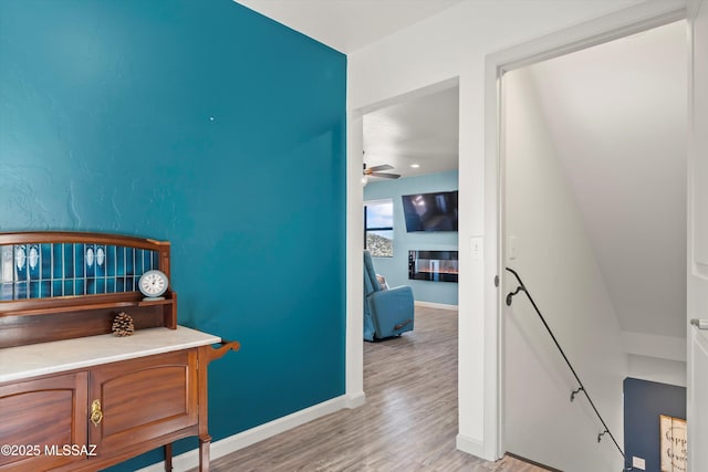 office area featuring a ceiling fan, a glass covered fireplace, light wood-style flooring, and baseboards