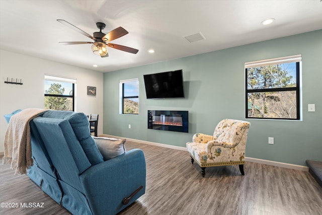 living room featuring a wealth of natural light, a glass covered fireplace, and baseboards