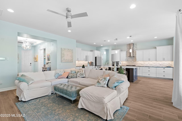 living room featuring ceiling fan with notable chandelier and light hardwood / wood-style floors