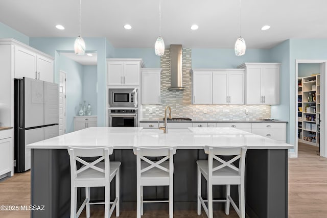 kitchen featuring wall chimney exhaust hood, white cabinetry, stainless steel appliances, and a kitchen island with sink