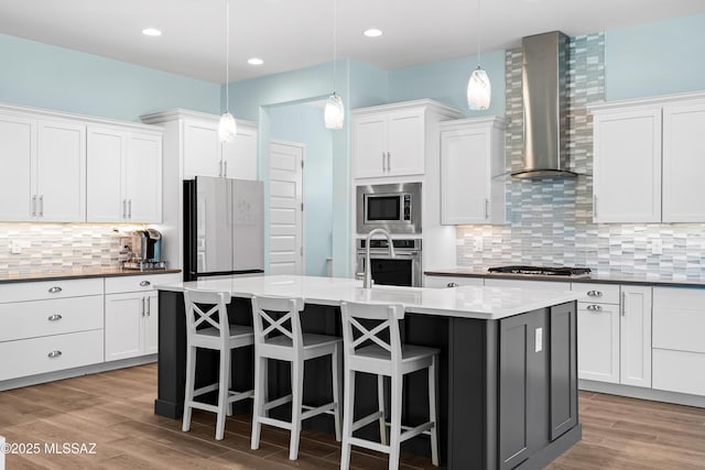 kitchen featuring white cabinetry, wall chimney range hood, decorative light fixtures, and stainless steel appliances