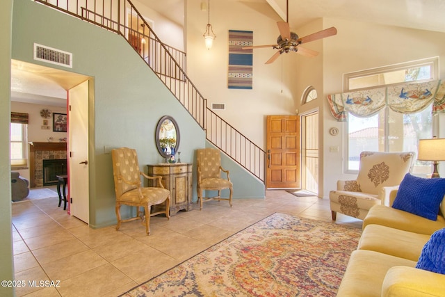 tiled living room featuring stairs, a tiled fireplace, a towering ceiling, and visible vents