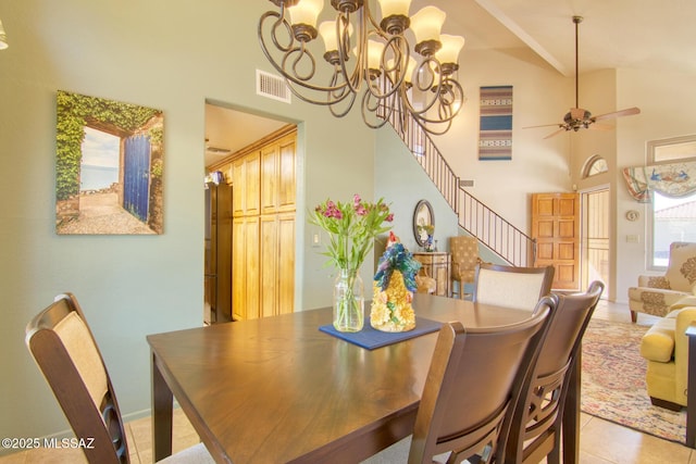 dining area featuring light tile patterned floors, visible vents, a ceiling fan, a towering ceiling, and stairs