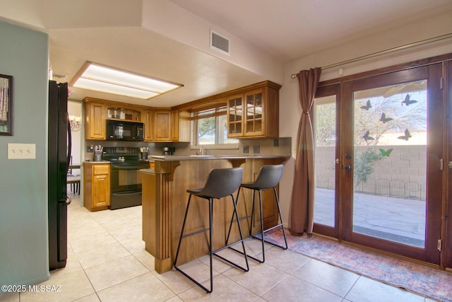 kitchen featuring light tile patterned flooring, a peninsula, visible vents, a kitchen breakfast bar, and black appliances