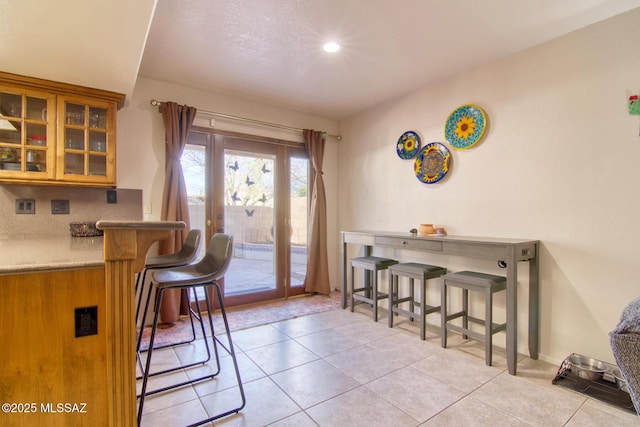 kitchen featuring glass insert cabinets, light tile patterned flooring, a breakfast bar area, and tasteful backsplash