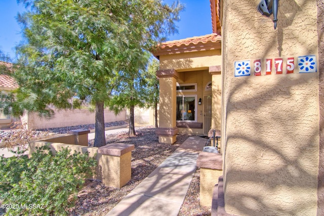 entrance to property featuring a tiled roof, fence, and stucco siding