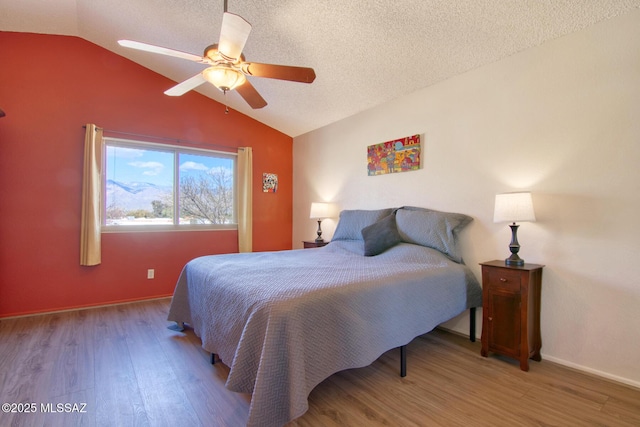 bedroom featuring baseboards, lofted ceiling, ceiling fan, wood finished floors, and a textured ceiling