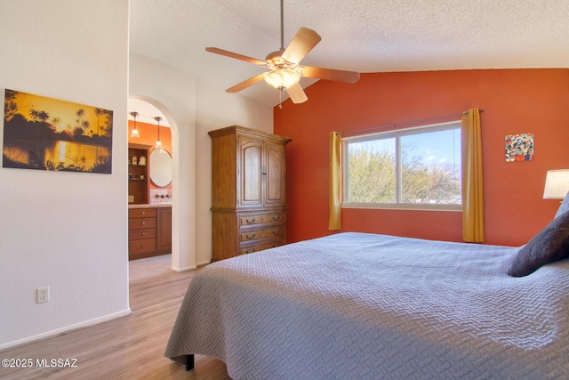 bedroom featuring lofted ceiling, ceiling fan, a textured ceiling, connected bathroom, and light wood-type flooring