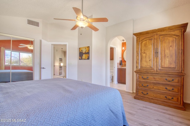 bedroom featuring arched walkways, ceiling fan, connected bathroom, visible vents, and light wood-type flooring