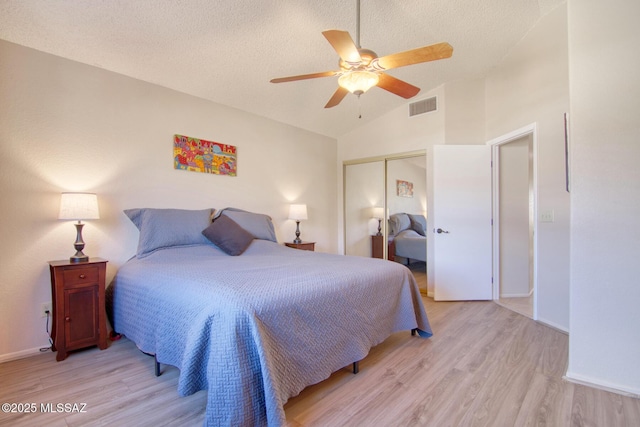 bedroom featuring light wood-style flooring, visible vents, vaulted ceiling, and a closet