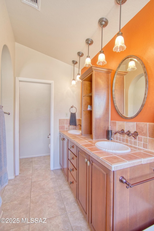 full bath with double vanity, vaulted ceiling, a sink, and tile patterned floors