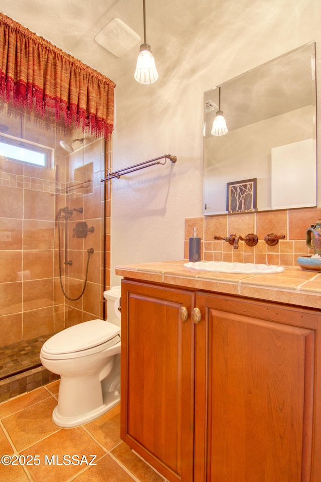 bathroom with tile patterned flooring, toilet, vanity, tiled shower, and tasteful backsplash