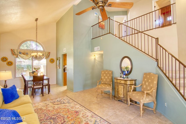 living area featuring stairs, visible vents, a high ceiling, tile patterned flooring, and ceiling fan with notable chandelier