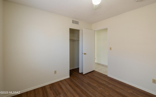 unfurnished bedroom with baseboards, visible vents, wood finished floors, a textured ceiling, and a closet