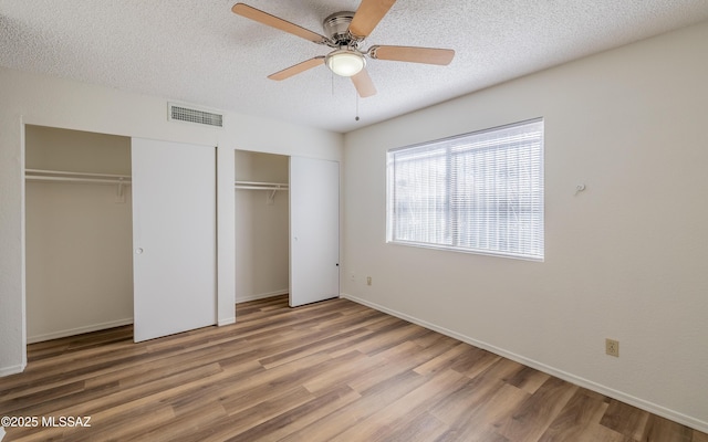 unfurnished bedroom featuring a textured ceiling, wood finished floors, visible vents, and multiple closets