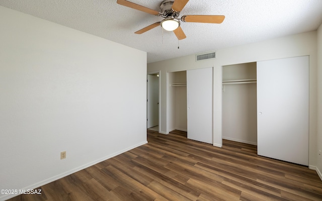 unfurnished bedroom featuring baseboards, visible vents, wood finished floors, a textured ceiling, and multiple closets