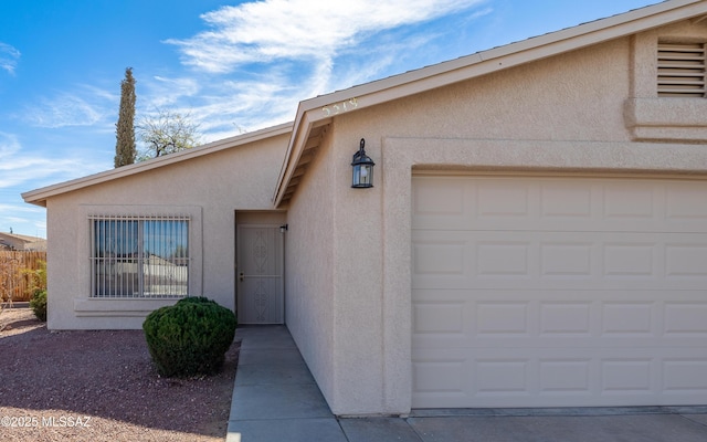 entrance to property featuring driveway, an attached garage, and stucco siding