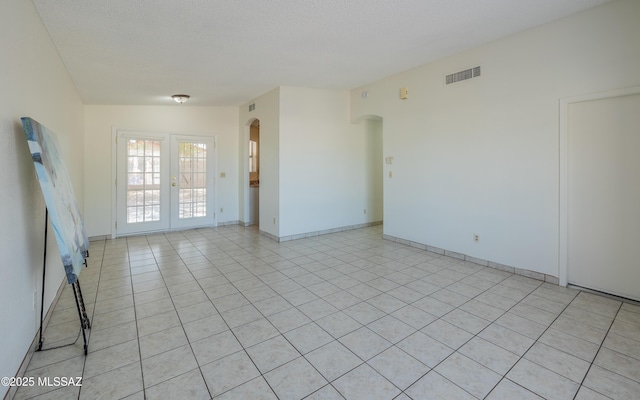 unfurnished room featuring visible vents, arched walkways, a textured ceiling, and light tile patterned flooring