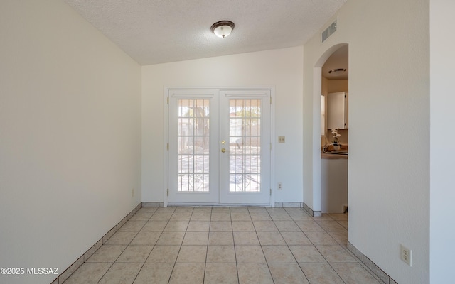 doorway with french doors, light tile patterned floors, lofted ceiling, visible vents, and a textured ceiling