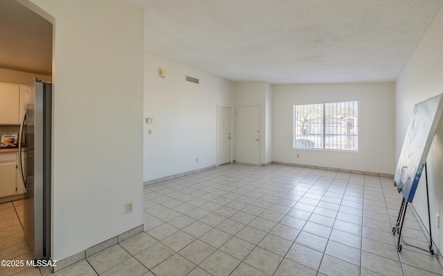 spare room featuring lofted ceiling, visible vents, a textured ceiling, and light tile patterned floors