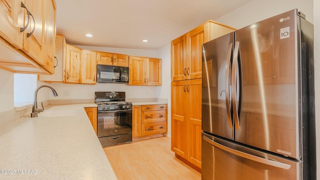 kitchen with sink, light brown cabinets, black appliances, and light wood-type flooring