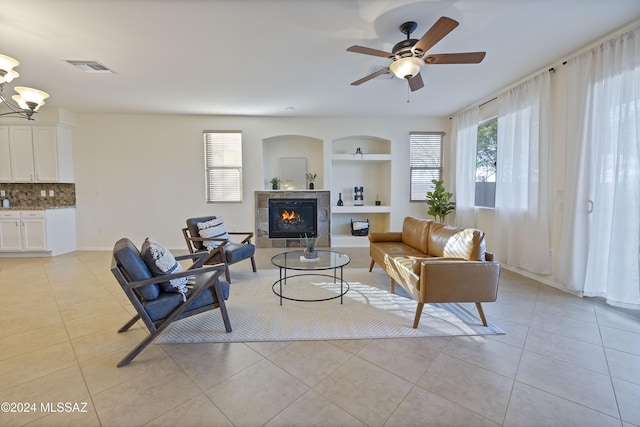 living room featuring light tile patterned floors, built in shelves, a fireplace, and ceiling fan