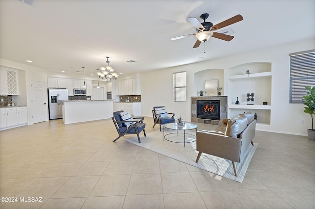 tiled living room with built in shelves, a fireplace, and ceiling fan with notable chandelier