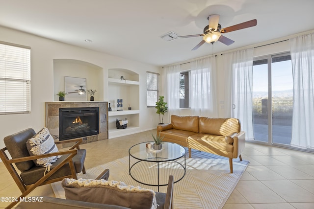 tiled living room featuring ceiling fan, built in shelves, a fireplace, and a healthy amount of sunlight