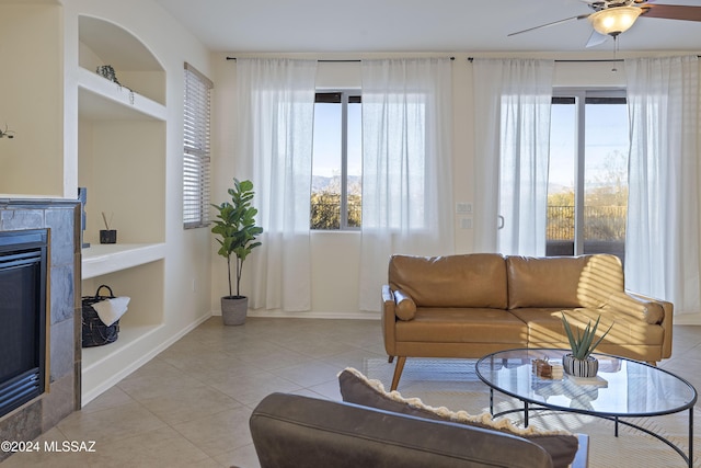 tiled living room featuring built in shelves, a tile fireplace, and ceiling fan