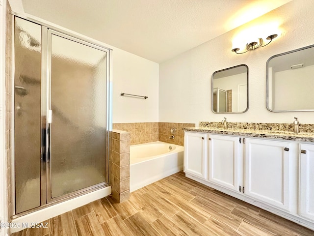 full bathroom with wood finish floors, a garden tub, double vanity, a stall shower, and a sink