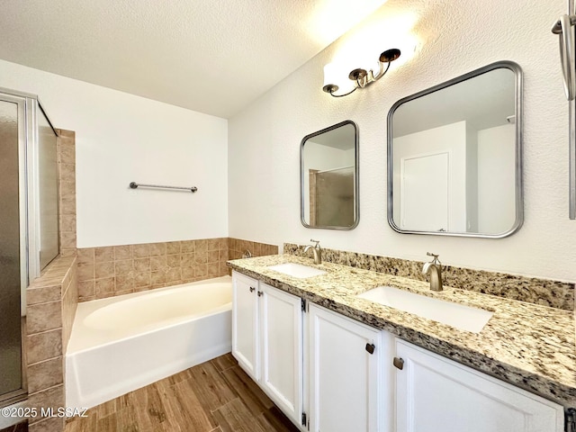 full bathroom featuring a sink, a textured ceiling, wood finished floors, and a bath