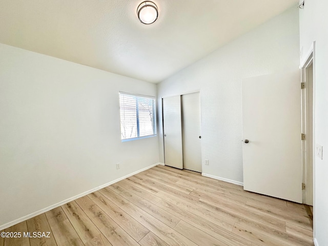 unfurnished bedroom with vaulted ceiling, light wood-style floors, a closet, and baseboards