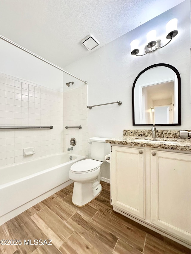 bathroom featuring wood finish floors, toilet, shower / bath combination, vanity, and a textured ceiling