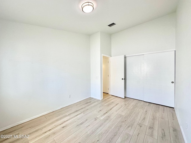 unfurnished bedroom featuring visible vents, baseboards, a closet, and wood finished floors