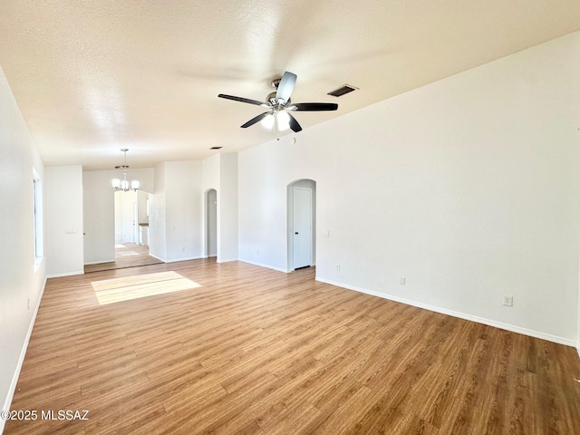 empty room featuring light wood finished floors, visible vents, ceiling fan with notable chandelier, arched walkways, and a textured ceiling