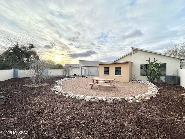 back of property at dusk featuring stucco siding, central AC unit, and fence