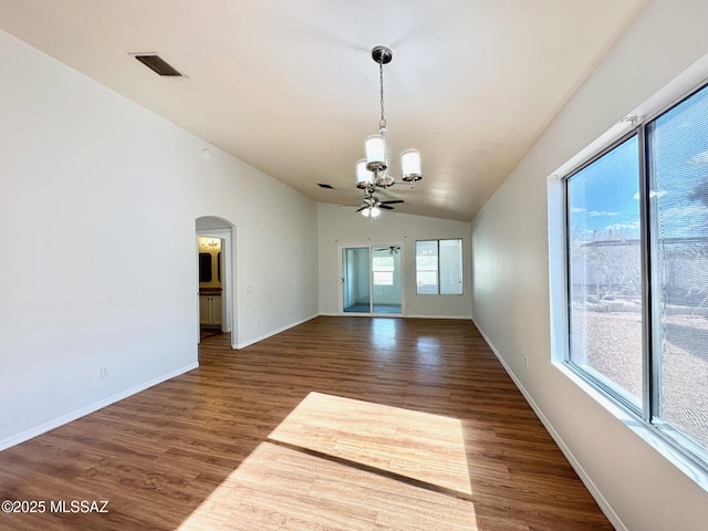 empty room featuring wood finished floors, baseboards, visible vents, lofted ceiling, and arched walkways