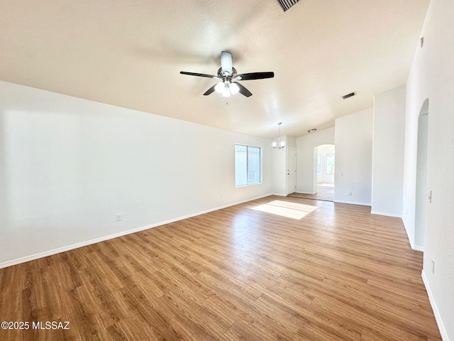 spare room featuring visible vents, baseboards, ceiling fan with notable chandelier, light wood-style floors, and arched walkways