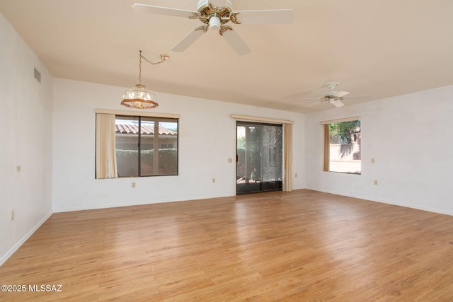 spare room featuring visible vents, light wood-style flooring, baseboards, and ceiling fan with notable chandelier