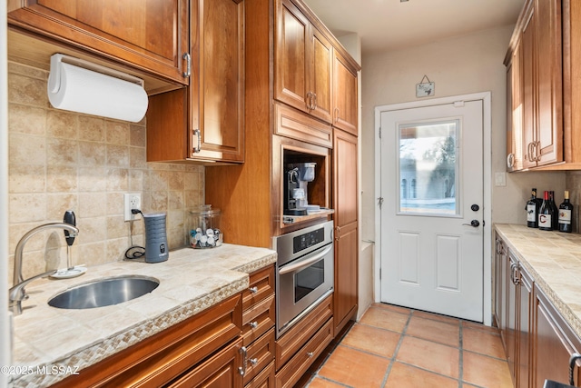 kitchen featuring sink, oven, backsplash, light tile patterned floors, and light stone counters