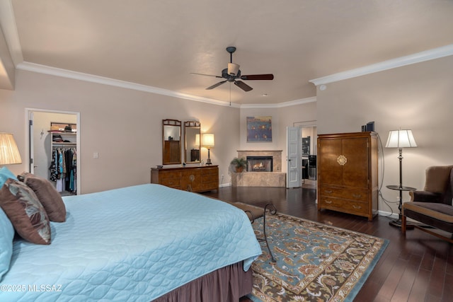 bedroom with a spacious closet, ornamental molding, dark hardwood / wood-style flooring, ceiling fan, and a premium fireplace