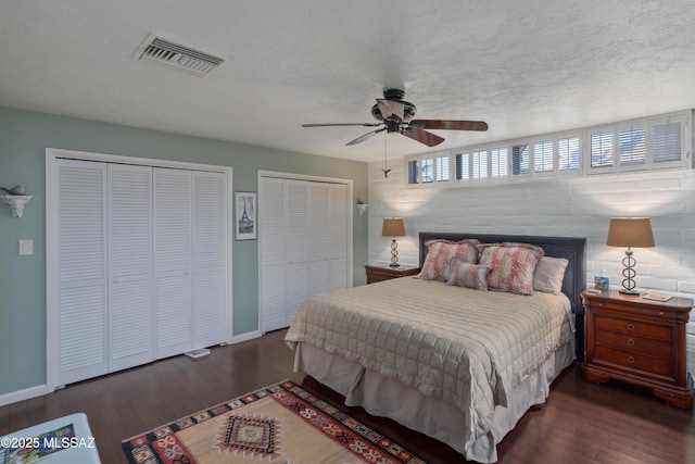 bedroom with ceiling fan, dark hardwood / wood-style floors, a textured ceiling, and two closets