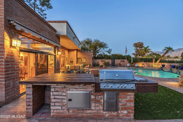 patio terrace at dusk with a fenced in pool, an outdoor kitchen, grilling area, and a bar