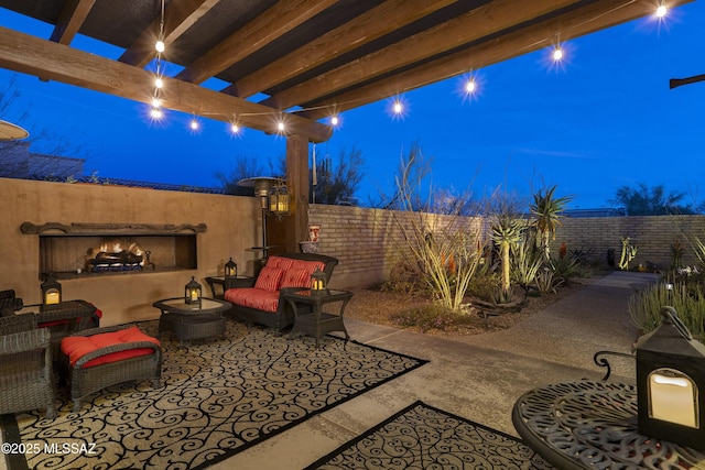 patio at twilight featuring a warm lit fireplace, a fenced backyard, and a pergola