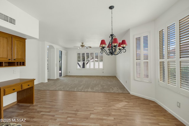 unfurnished dining area featuring ceiling fan with notable chandelier and light hardwood / wood-style floors