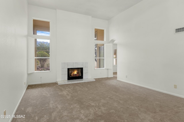 unfurnished living room featuring a tiled fireplace, light colored carpet, and a towering ceiling