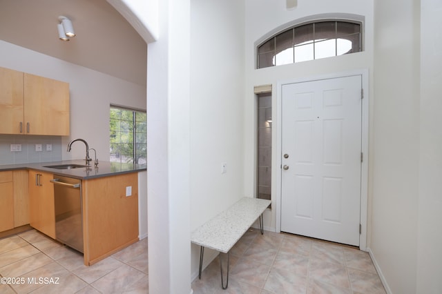 kitchen with light brown cabinets, light tile patterned flooring, arched walkways, a sink, and stainless steel dishwasher