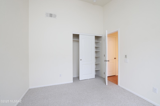 unfurnished bedroom with visible vents, baseboards, carpet, a towering ceiling, and a closet