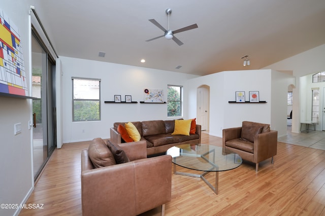 living area with arched walkways, light wood-type flooring, and a ceiling fan