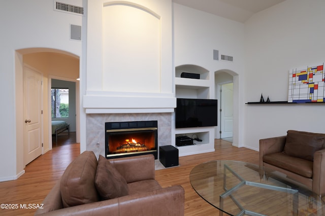 living room featuring arched walkways, visible vents, light wood-style flooring, and a fireplace